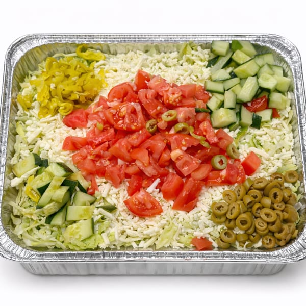 Large catering tray of salad with shredded lettuce, cheese, tomatoes, cucumbers, olives, and peppers.