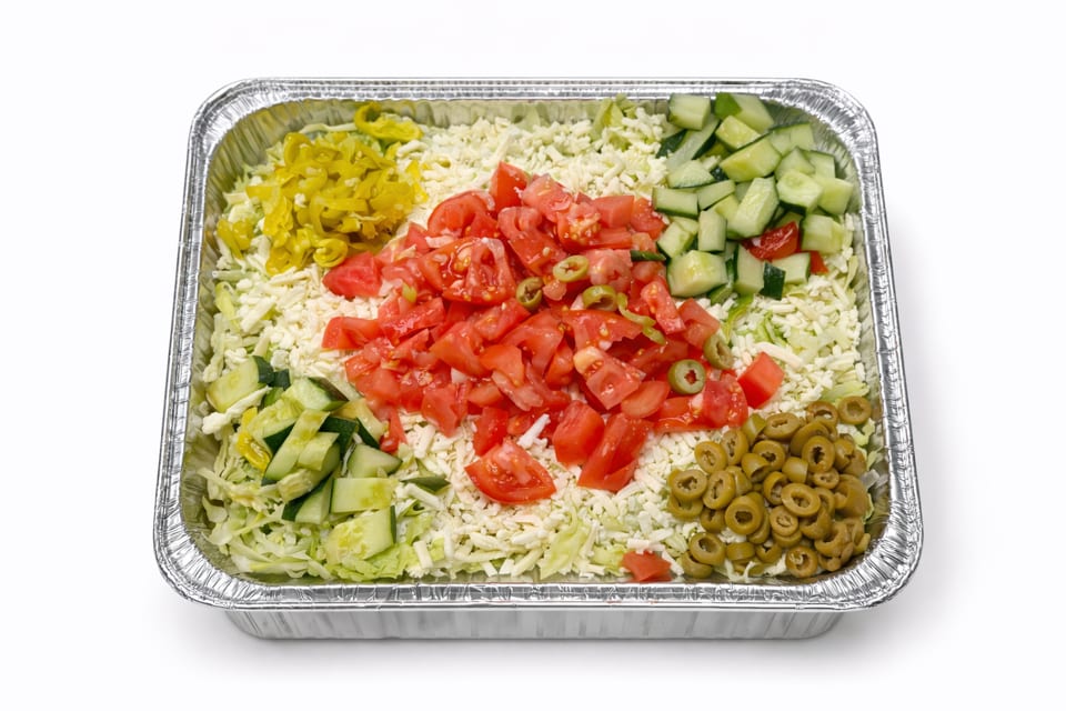 Large catering tray of salad with shredded lettuce, cheese, tomatoes, cucumbers, olives, and peppers.