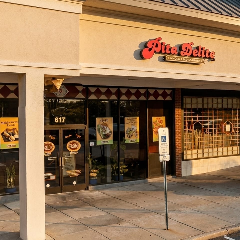 The exterior of Pita Delite restaurant, with large windows displaying food advertisements and a brick pillar.