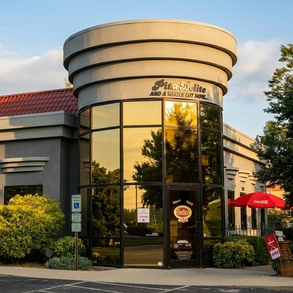 Exterior of Pita Delite restaurant with a red tile roof, large windows, and a red Coca-Cola umbrella.