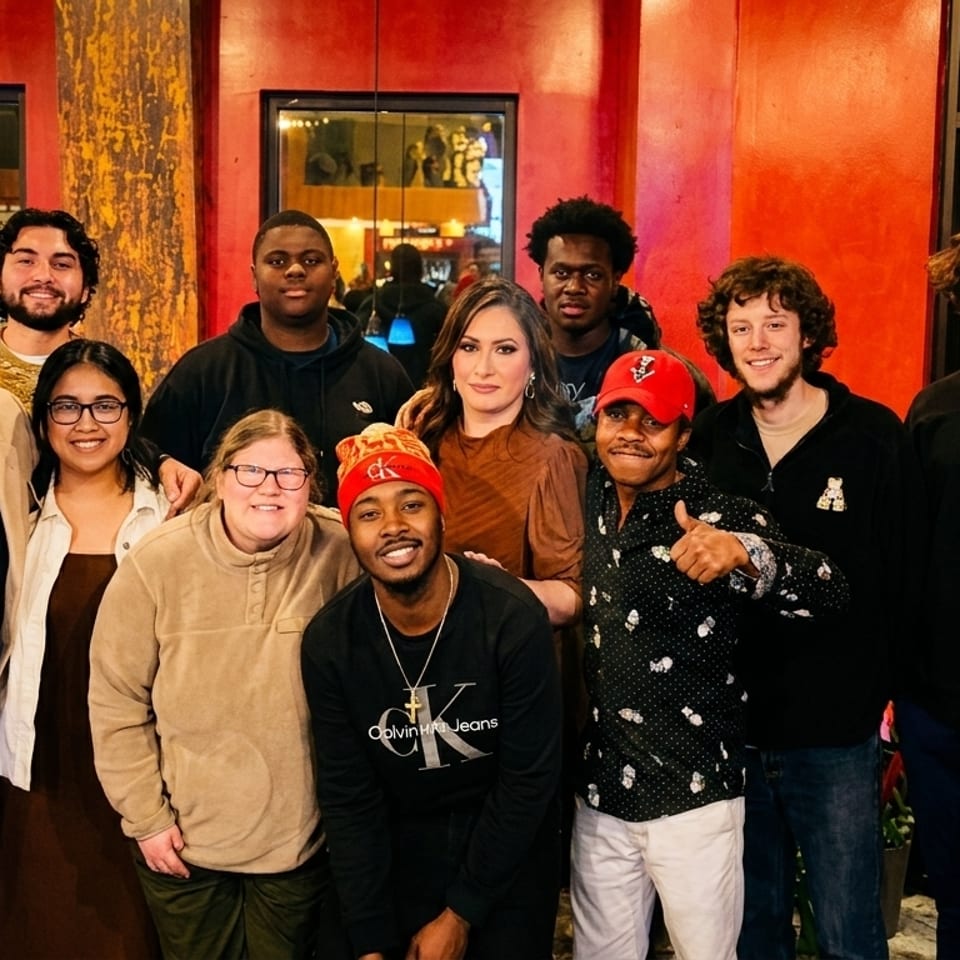 A large group of diverse people smiling for a photo inside a restaurant with red walls.