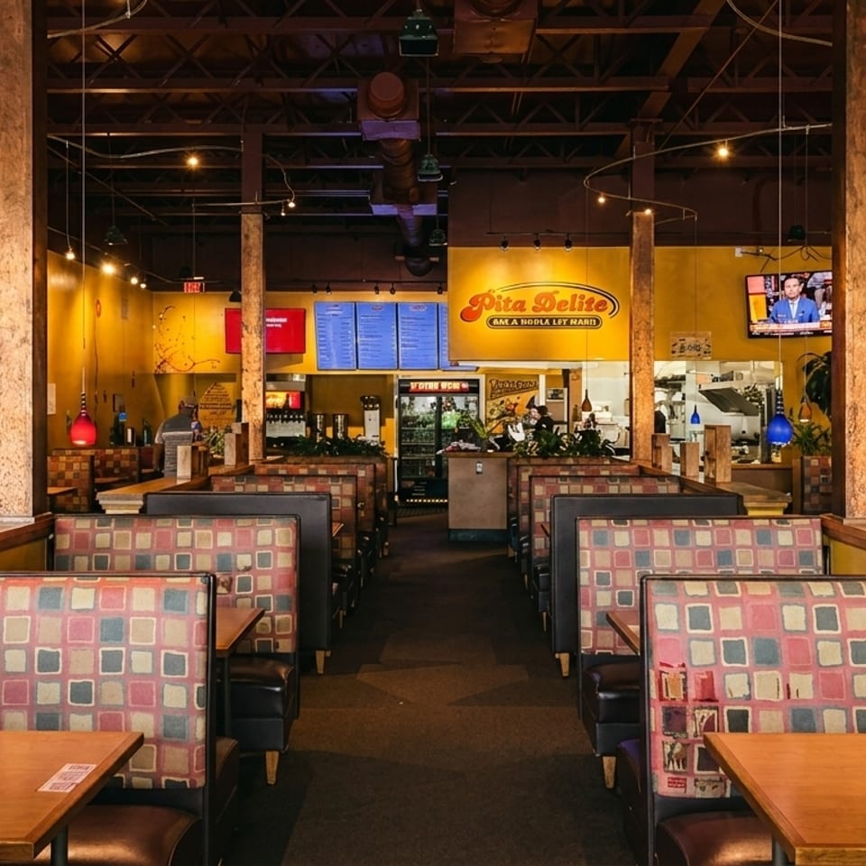 Interior of Pita Delite restaurant with rows of booths, yellow walls, and a menu board.