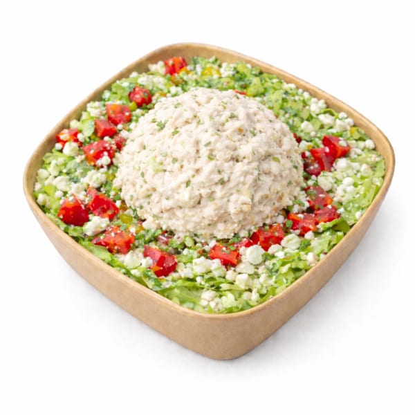 Tuna salad scoop surrounded by chopped lettuce, red peppers, and feta cheese in a brown bowl.